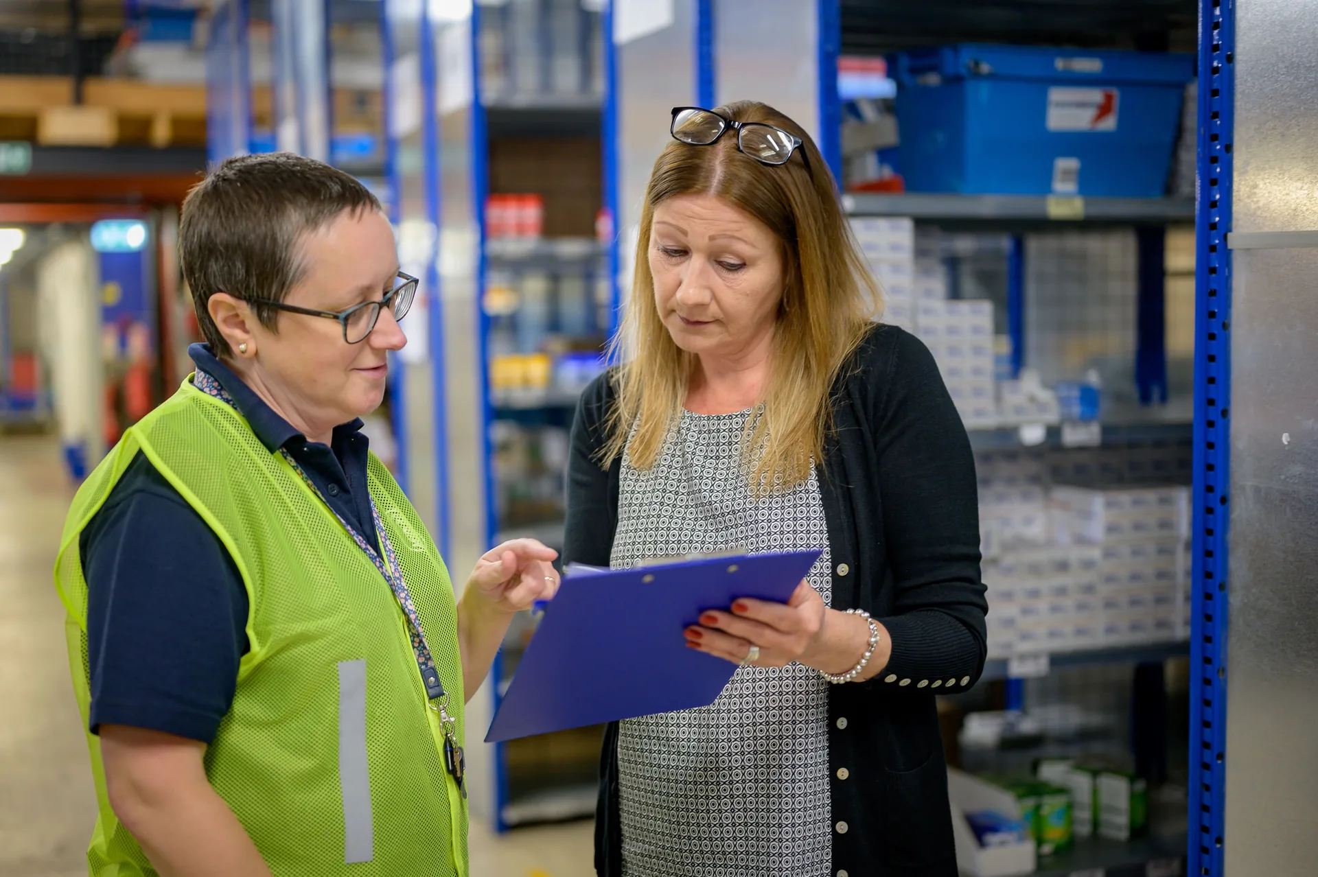 Two workers reviewing a clipboard in a warehouse aisle