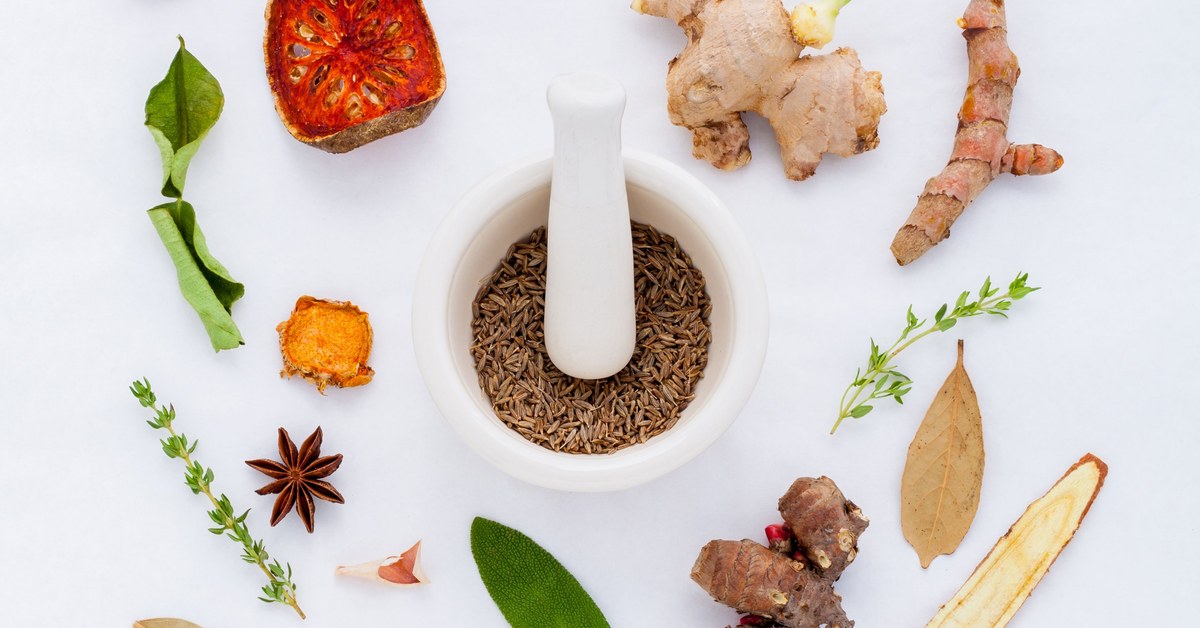 Spices, herbs, roots, and seeds arranged around a mortar and pestle